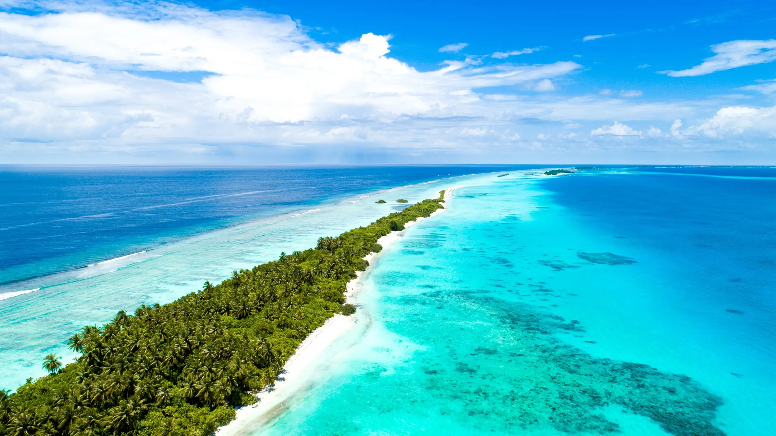 aerial shot, narrow island covered by tropical trees, the Middle Sea, Maldives